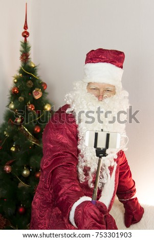 Santa Claus takes pictures of himself.
In the room near the Christmas tree, Santa Claus is holding a self-stick and taking pictures of himself in different ways.