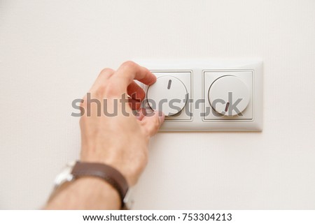 Saving energy concept: Human hand turning down electrical light dimmer switch. Royalty-Free Stock Photo #753304213