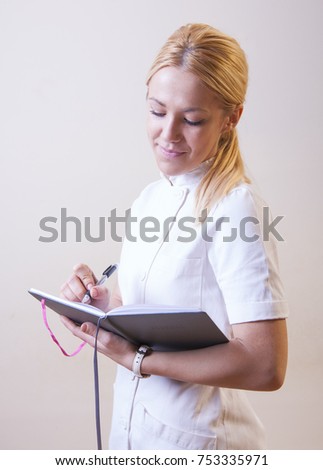 Young blonde nurse taking notes and holding a syringe wearing a watch. Putting makeup on while holding a mirror. Wearing white nurse coat / uniform.