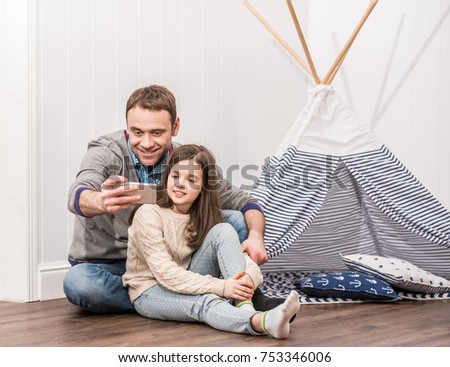 Father and daughter taking selfie playing at home with constructed wigwam