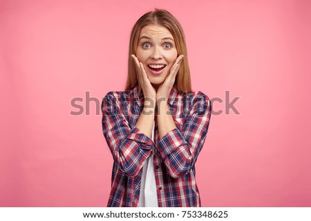 Beautiful amazed woman can`t believe her eyes, glad to recieve unexpected present from boyfriend, has happy and surprised expression, poses against pink studio background. Happiness concept.