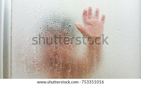 hand pressed on the bathtub glass.boy hand and unrecognizable silhouette behind wet glass in shower.