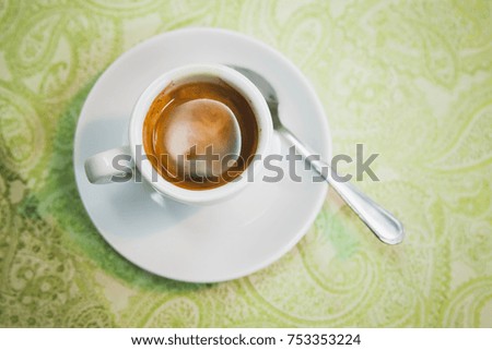 Freshly brewed espresso coffee in white cup stands on table, top view. Closeup photo with selective focus