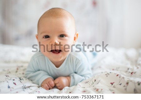 Adorable baby boy in white sunny bedroom in winter morning. Newborn child relaxing in bed. Family morning at home. Newborn kid during tummy time smiling happily at home Royalty-Free Stock Photo #753367171