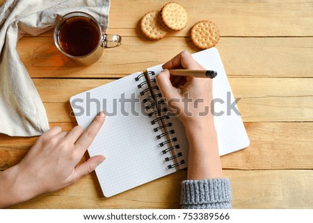 Women hands open notebook with cup of tea, cake on the wooden desk