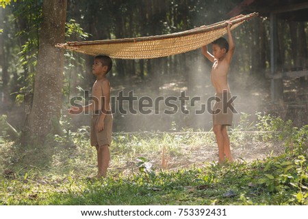 Two brothers standing by with a bamboo boat on a head in rural Thailand.