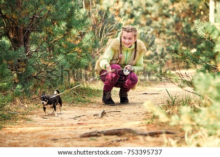 girl outdoors with a small dog.smiling girl relaxing with dog.Beautiful girl smiling in a jacket and cap with the little dog a Chihuahua puppy. the child holds the leash on your dog  on the nature.
