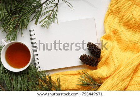 Christmas background with a Cup of tea, a notebook, fir cones, branches of pine with large needles and a yellow sweater. Top view, close-up 
