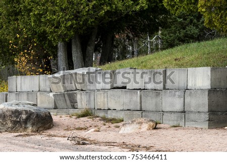 A concrete retaining wall that is falling over. Grass is above the wall, sand below. Several blocks are pushed out and leaning over.