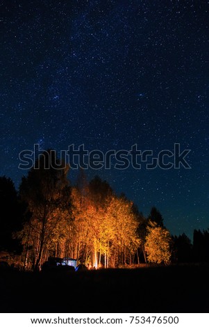 Travelers have a rest in his camp at night near campfire and tent under beautiful night sky full of stars. Recreation and outdoor photo. 