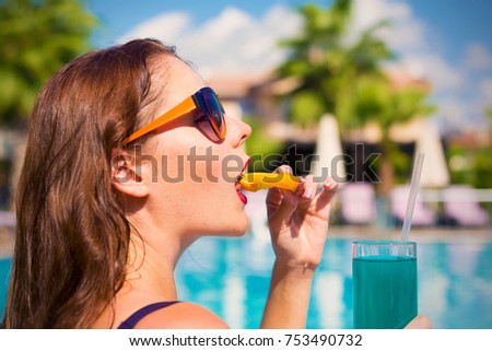 Young woman in sunglasses drink alcohol cocktail with orange on a swimming pool
