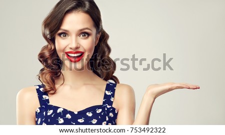 Woman surprise showing product .Beautiful girl  with curly hair and red lips pointing to the side . Presenting your product. Expressive facial expressions