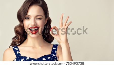 Pin-up retro girl with curly hair  winking, smiling and showing OK sign . Presenting your product. Expressive facial expressions
 Royalty-Free Stock Photo #753493738