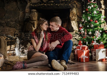 Happy couple sits near fireplace in chalet. Christmas decorated room