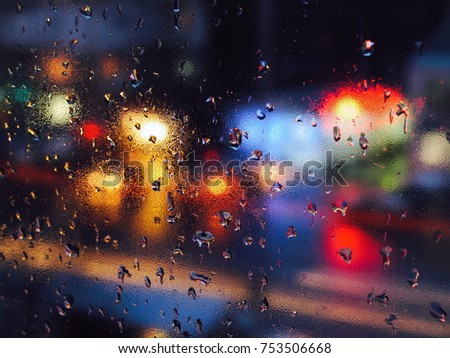 Rain drops on a window during the rain in a city. Background with blurred lights from cars on the road. Lights of different colors.