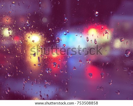Drops of water during the rain in a city. Rain drops cover the window glass, a blurred city lights are on the background. Lights of different colors.