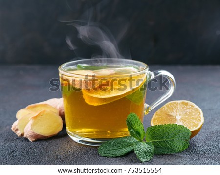 Herbal tea with ginger, mint and lemon. Hot tea glass cup with steam and ingredients on black cement background. Copy space