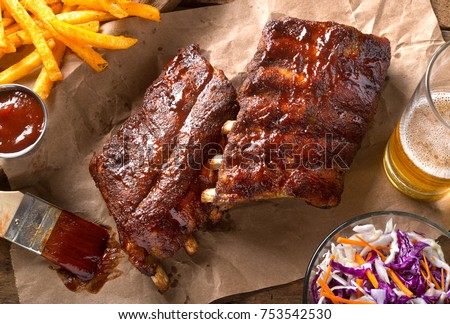 A rack of delicious baby back ribs with barbecue sauce, french fries, coleslaw and beer. Royalty-Free Stock Photo #753542530
