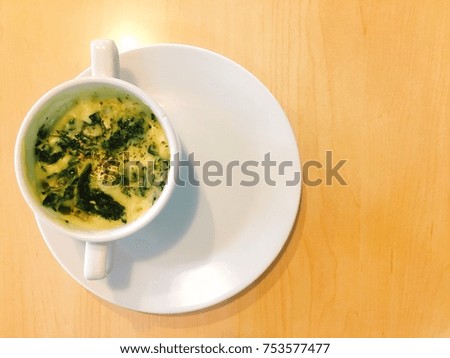 Spinach with cheese in white cup and plate on wood table. It is Italian food. Concept for restaurant business with space for text design. Blurry picture and over exposure.