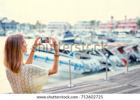 Tourism concept. Young woman  taking photo on smartphone while standing on the marine seafront.
