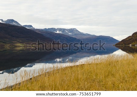 Scenic landscape photo of mountains and reflective lake on a cloudy day in Norway.