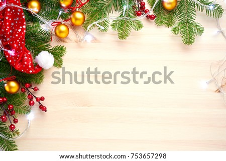 Christmas background decoration with lights, balls, santa hat and fir tree branches flat lay on wooden texture. Top view with blank space.