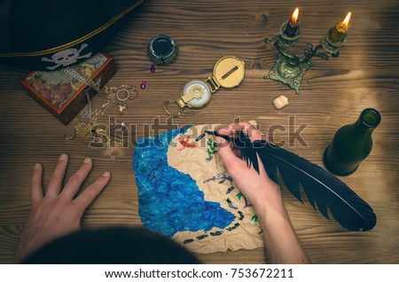 Treasure map, compass,male hands and pirate hat on wooden table. Treasure hunt. Adventurer. The pirate draws mark on treasure map where he buried the awarded treasures.