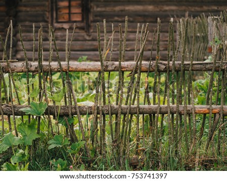 Traditional Belarusian pole fence of vertical wooden sticks in front of old national house. Belarusian village