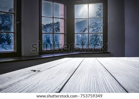 Wooden table of free space for your decoration. Background of window and view of mountains and moon on the sky with few stars. Santa claus home interior. 