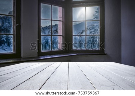 Wooden table of free space for your decoration. Background of window and view of mountains and moon on the sky with few stars. Santa claus home interior. 