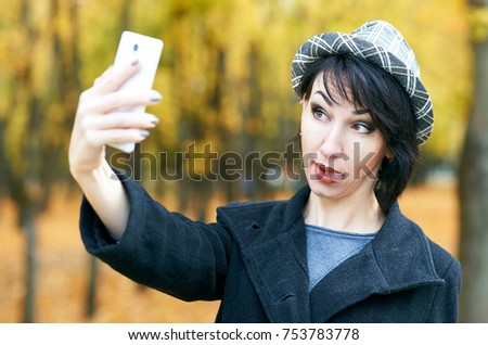 girl taking selfie and show tongue, autumn city park, yellow leaves and trees, fall season