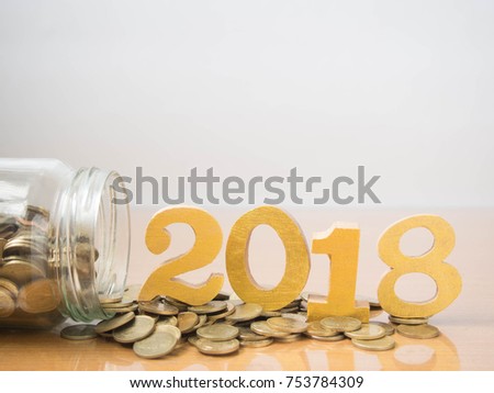 New year saving money and financial planning concept. Coins spilling out of glass bottle w/ gold wooden number 2018 on table. Idea for business growth, tax payment, investment and banking. Copy space. Royalty-Free Stock Photo #753784309