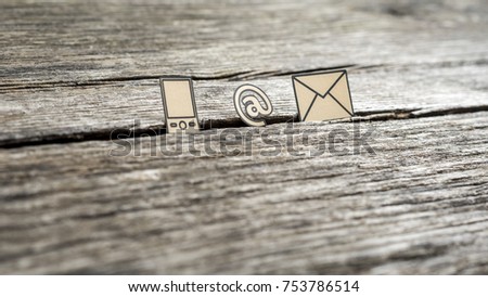 Contact icons at sign, mail and mobile phone outlined with black stuck in between a crack in the wooden surface.