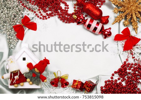 Christmas frame background with decorative elements. Ceramic house, souvenir dolls, star, decorative bells, gifts, snowflakes, garlands and decorations on white silk cloth. Top view with copy space.