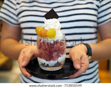 Holds glass of mixed berry parfait topped with whipped cream and sliced fresh grape, Japanese shaved ice dessert flavored. Healthy eating concept. Selective focus.