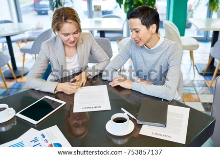 High angle portrait of two happy businesswomen signing contract sitting at table in modern office and smiling