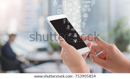Woman hands holding and using smartphone with black screen and social media doodle icon on blurred office space interior background.