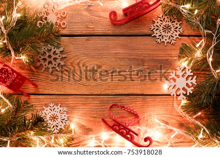 Picture on top of wooden surface with burning garland, branches of spruce, Christmas toys, snowflakes. Empty place for text.