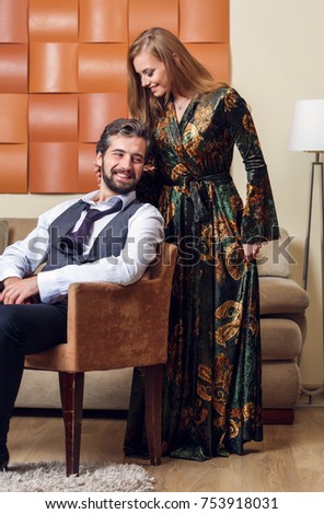 Photo of businessman on chair and long-haired blonde in dress in room at afternoon