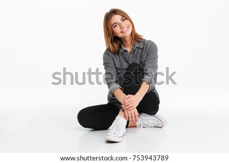 Portrait of a pretty cheery girl sitting and looking at camera isolated over white background