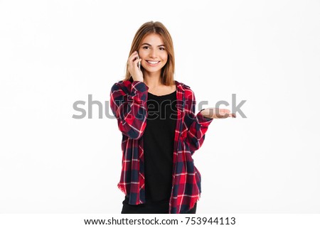 Portrait of a smiling pretty girl talking on mobile phone while holding copy space on her palm and looking at camera isolated over white background