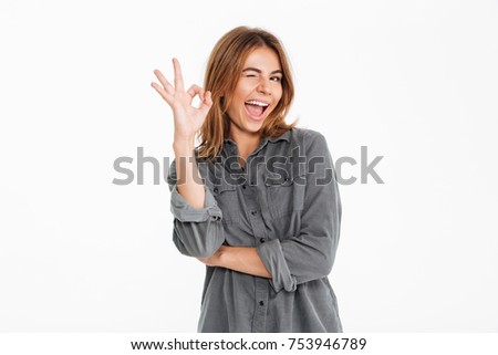 Portrait of a happy excited girl showing ok gesture and winking isolated over white background