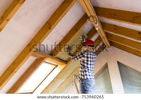 Man installing thermal roof insulation layer - using mineral wool panels. Attic renovation and insulation concept Royalty-Free Stock Photo #753960265