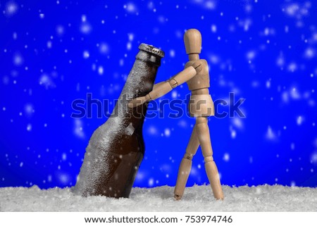 Frozen beer bottle in ice with falling snow on blue background