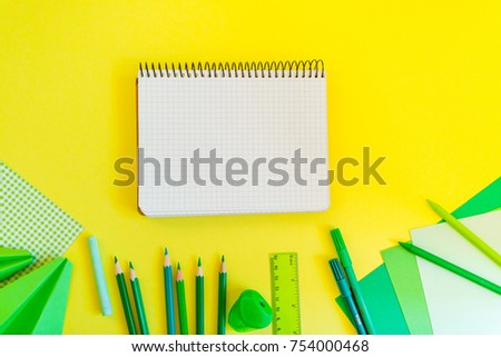 Creative, fashionable, minimalistic, school or office workspace with green supplies on yellow background. Flat lay. Bank paper spiral notebook on yellow background.