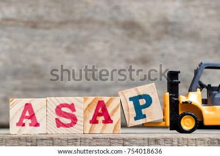 Yellow plastic forklift hold letter P to complete word ASAP (abbreviation of as soon as possible) on wood background