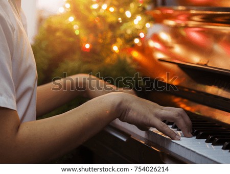 close up of man hands plays  on  Piano Keys with Christmas tree and decoration light, in the night of Christmas season, Christmas background