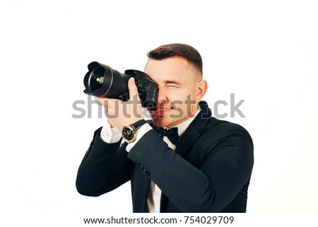 A young man with a camera in hands takes pictures on a white background