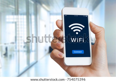 Close-up of hand holding smartphone with WiFi symbol and connect button on the screen to access public wireless internet, blurred building interior Royalty-Free Stock Photo #754075396