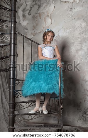 Girl in a smart blue dress with white at the spiral staircase.